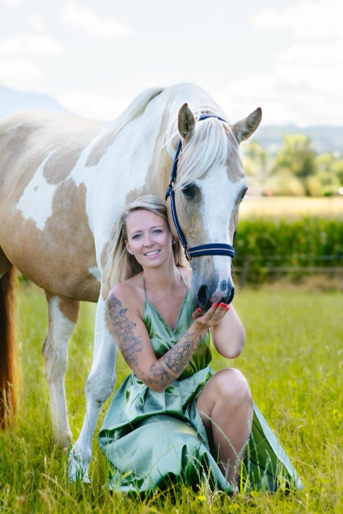 Cavalière assise dans l’herbe auprès de son cheval pie
