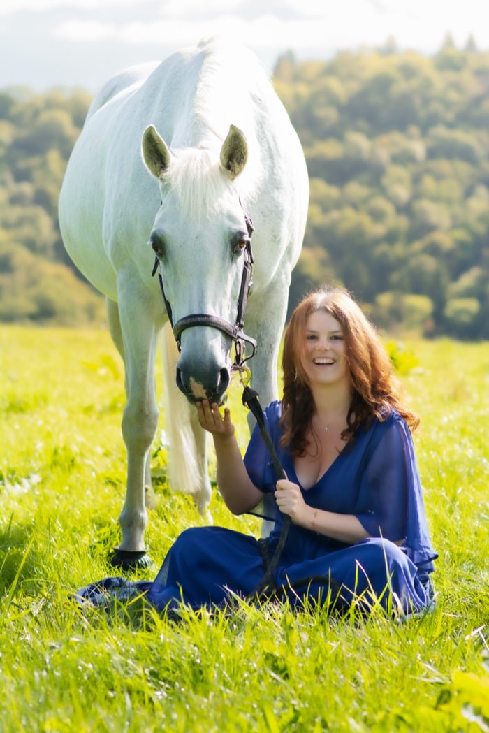 Cavalière en robe bleue assise près de sa jument grise